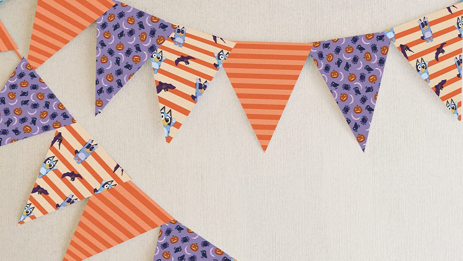 An image of colourful halloween bunting hanging on a wall. Patterns include bats, Bluey, pumpkins, orange and purple stripes and spiders.