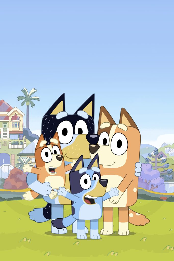 Bluey, Bingo, Mum and Dad stand together smiling in a bright outdoor setting with a clear blue sky.