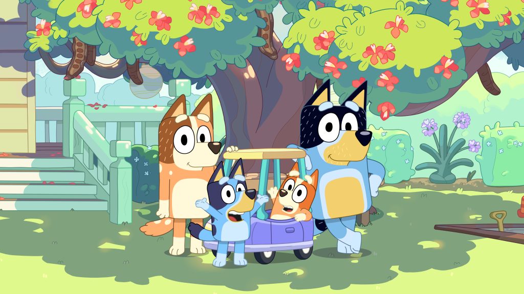 Bluey and her family gather around Bingo sitting in Pedley under a flowering tree in a garden.